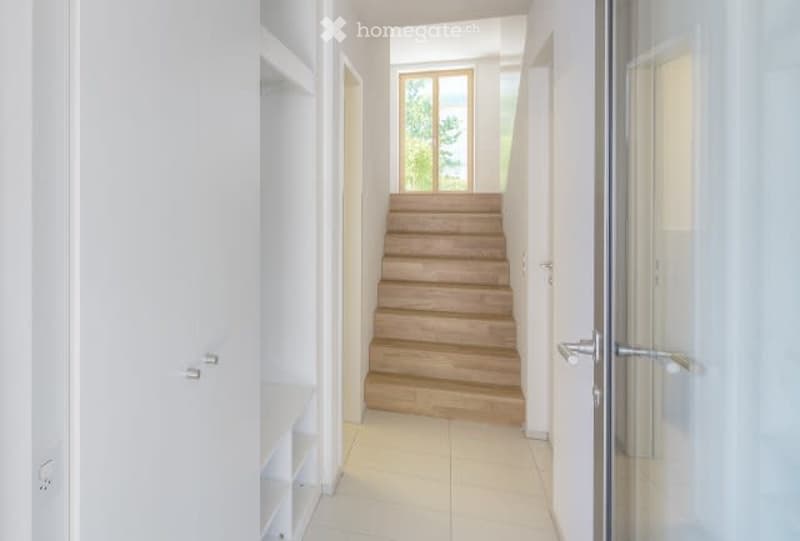 Empty hallway with white walls, wooden stairs, white floor, glass door, window