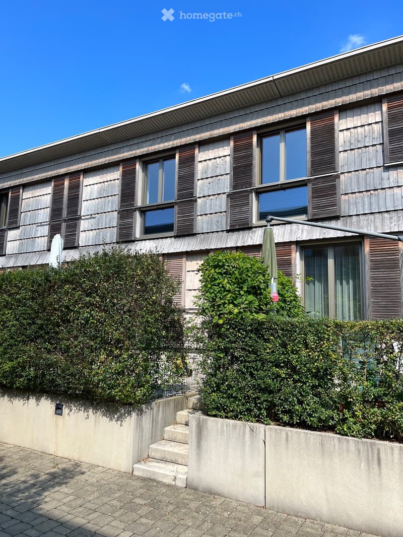 Wooden exterior, multiple windows, concrete steps, hedges, outdoor umbrella