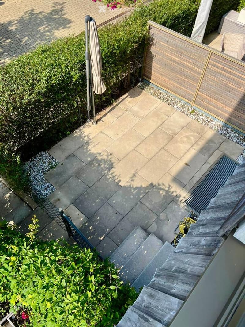 A small garden with a paved patio, wooden fence, and a closed umbrella.