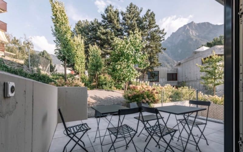Balcony with outdoor furniture, overlooking a landscaped garden and mountain view.