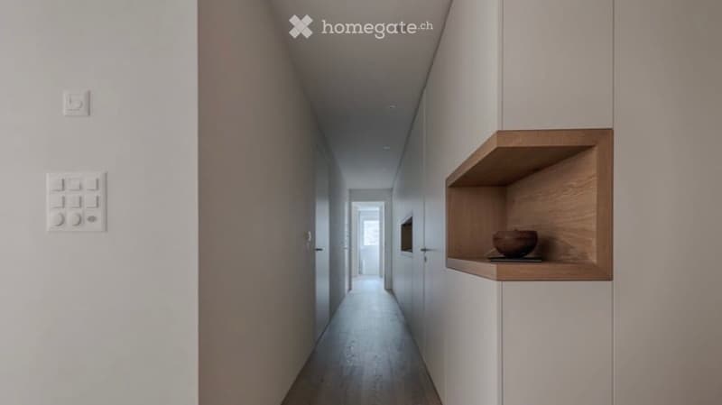 Modern hallway with white walls, wooden floor, built-in wooden shelf with a decorative bowl, and recessed lighting.