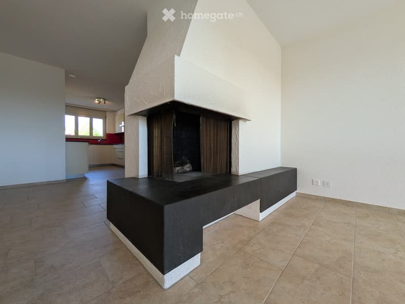 Modern living room with a built-in black bench seating, a fireplace with dark curtains, and a view into a kitchen area with white cabinets and red backsplash.