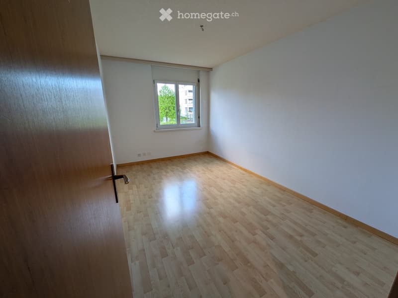 Empty room with wooden flooring, white walls, and a window with a view of greenery outside.