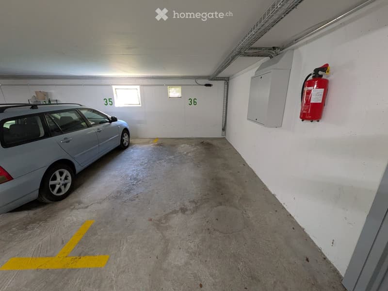 Underground parking space with a parked car, marked parking spots, and a fire extinguisher on the wall.