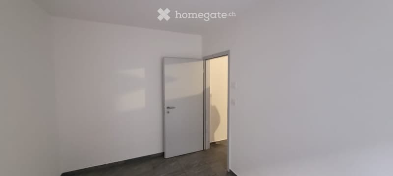 Empty room with white walls and dark tiled floor, featuring a closed door and an open doorway leading to another room.