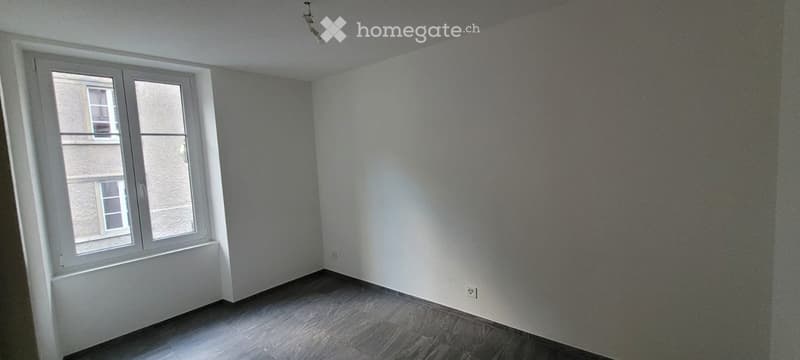 Empty room with light grey walls, wooden floor, and a large window with white frame. No furniture or equipment present.
