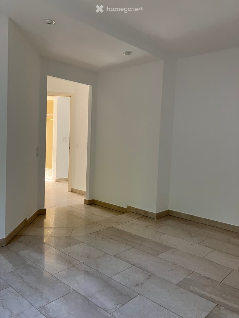 Empty hallway with tiled floor and light-colored walls, featuring a doorway leading to another room.