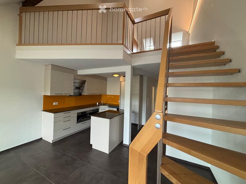Modern hallway with a wooden staircase leading to an upper level, featuring a kitchen area with white cabinets, a black countertop, and built-in appliances.