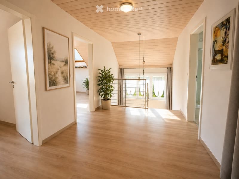 Bright hallway with wooden flooring, white walls, and modern lighting. Features include a large potted plant, framed artwork, and a glass railing leading to a sunlit area.