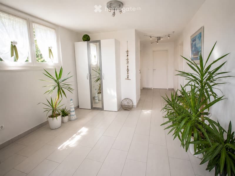 Bright hallway with white tiled flooring, large windows, potted plants, and a mirrored wardrobe.