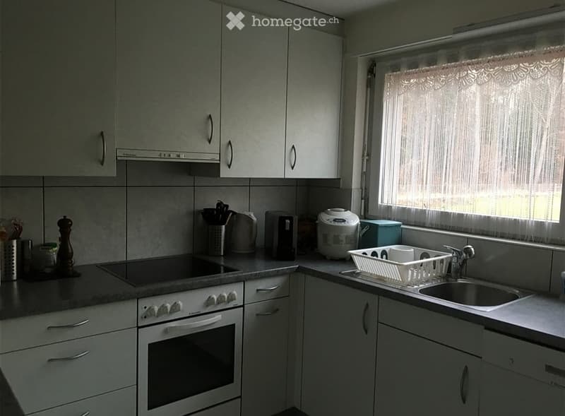 Modern kitchen with white cabinets, stainless steel appliances, and a window with curtains. Includes an oven, sink, dish rack, rice cooker, toaster, and various kitchen utensils.
