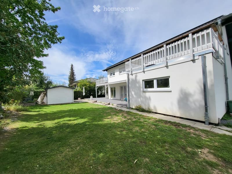 Two-story white house with a balcony, surrounded by a well-maintained lawn and trees.