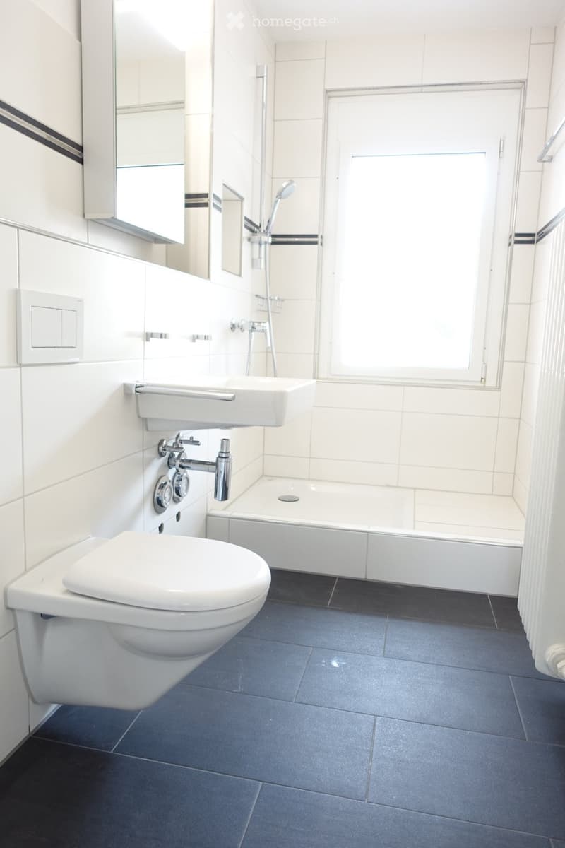 Modern bathroom with white tiles, a toilet, a sink, a bathtub, and a mirror cabinet.