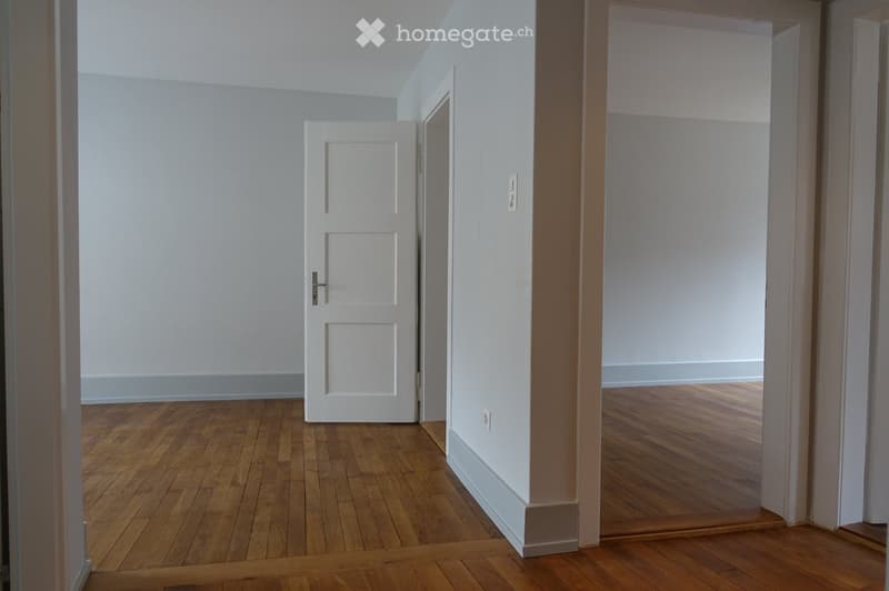Empty hallway with wooden flooring, white walls, and two doors leading to adjacent rooms.
