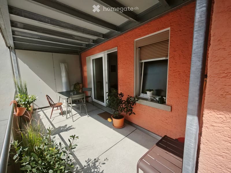 Balcony with a table, chairs, and potted plants, featuring a sliding glass door leading inside and a window with a blind.