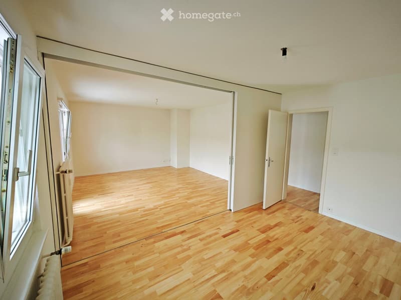 Empty room with wooden flooring, white walls, and multiple doors leading to other spaces.