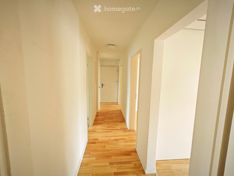 Empty hallway with light wooden flooring, white walls, and several doors leading to other rooms.