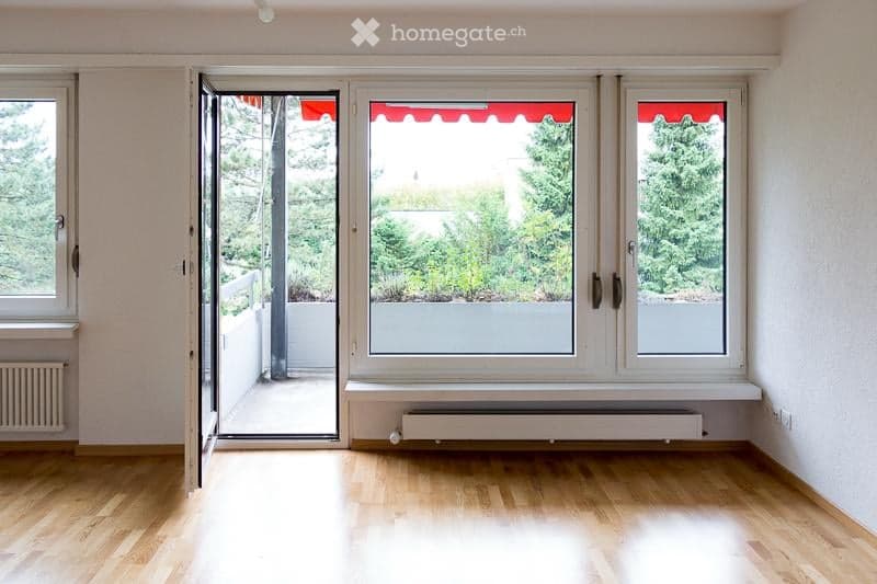 Empty room with wooden flooring, large windows, and an open sliding door leading to a balcony.