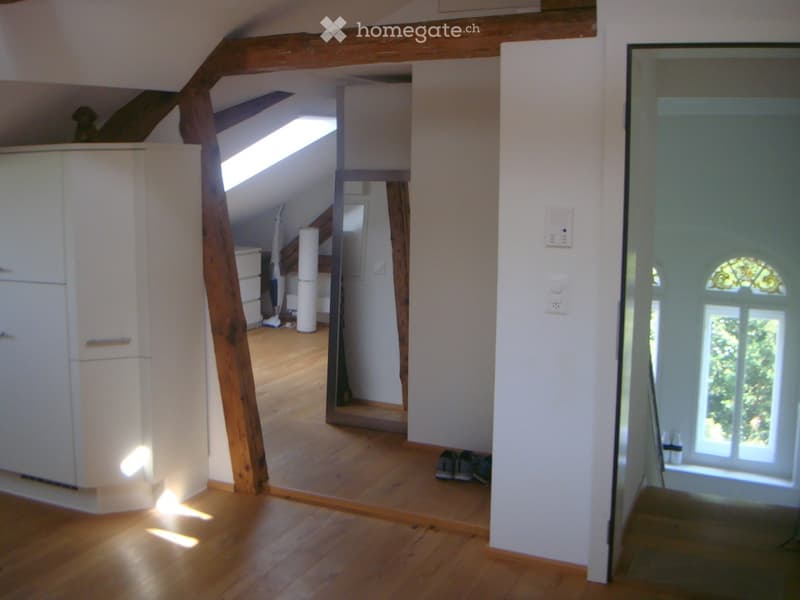 Bright, open attic space with wooden beams, wooden flooring, and large skylight windows. The room is empty, with no furniture or furnishings visible.