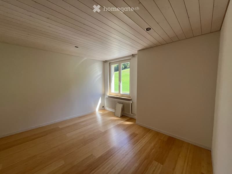 Empty room with wooden flooring, white walls, and a large window letting in natural light. A radiator is visible beneath the window.