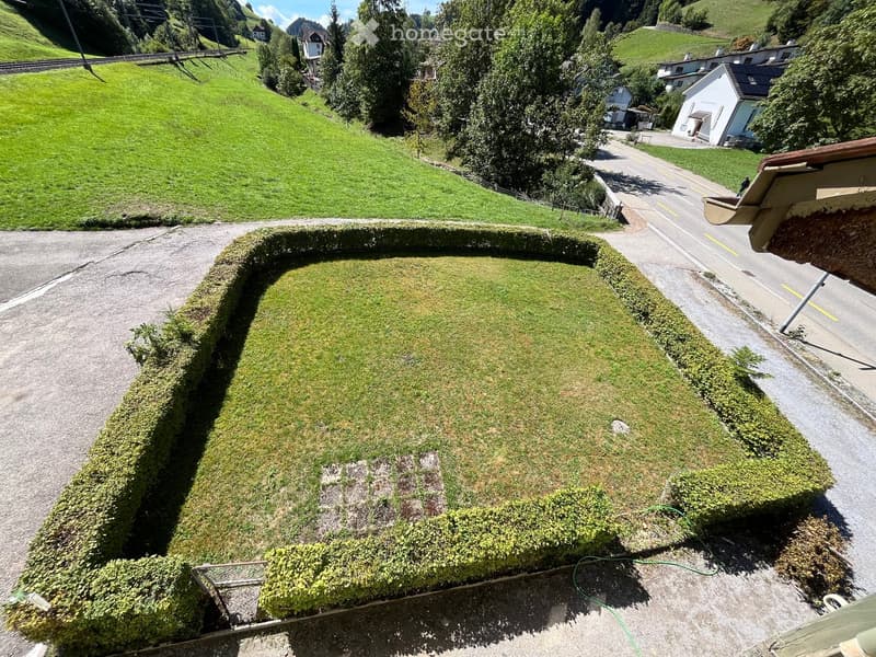 A well-maintained garden with neatly trimmed hedges, a gravel pathway, and a view of a road and surrounding greenery.