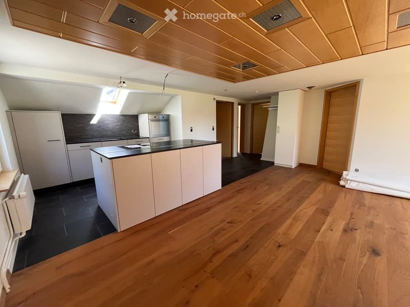 Modern kitchen with white cabinets, black countertop, and wooden flooring. Features an island with built-in oven and ample storage space.