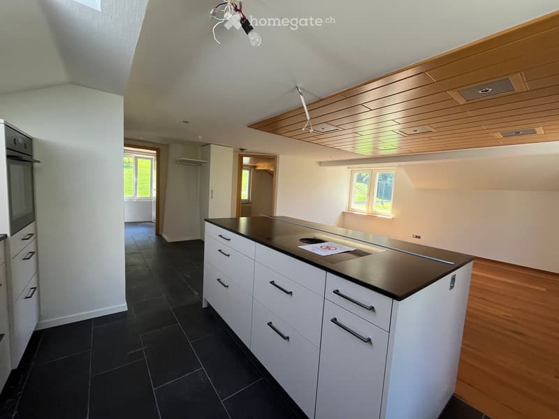 Modern kitchen with white cabinets, black countertop, and dark tiled floor. Features an integrated oven and a window with a view of greenery.