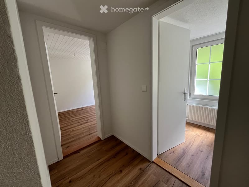 Empty hallway with wooden flooring, white walls, and two open doors leading to adjacent rooms.