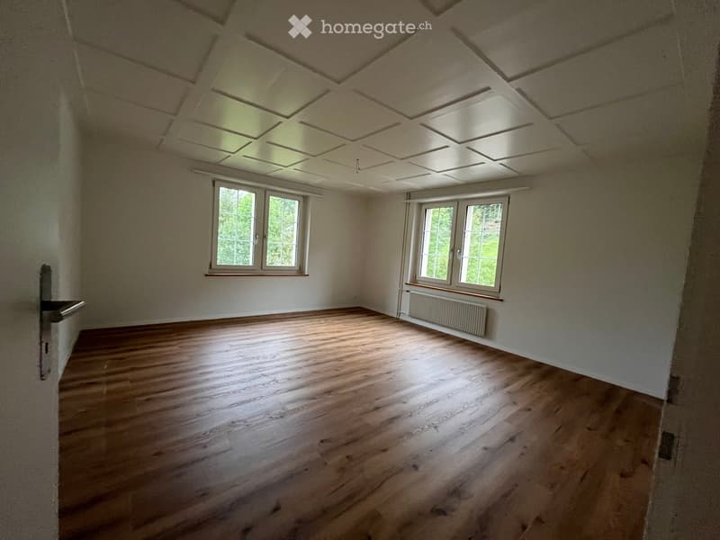 Empty room with wooden flooring, white walls, and two windows with white frames. The ceiling has a coffered design with recessed lighting.
