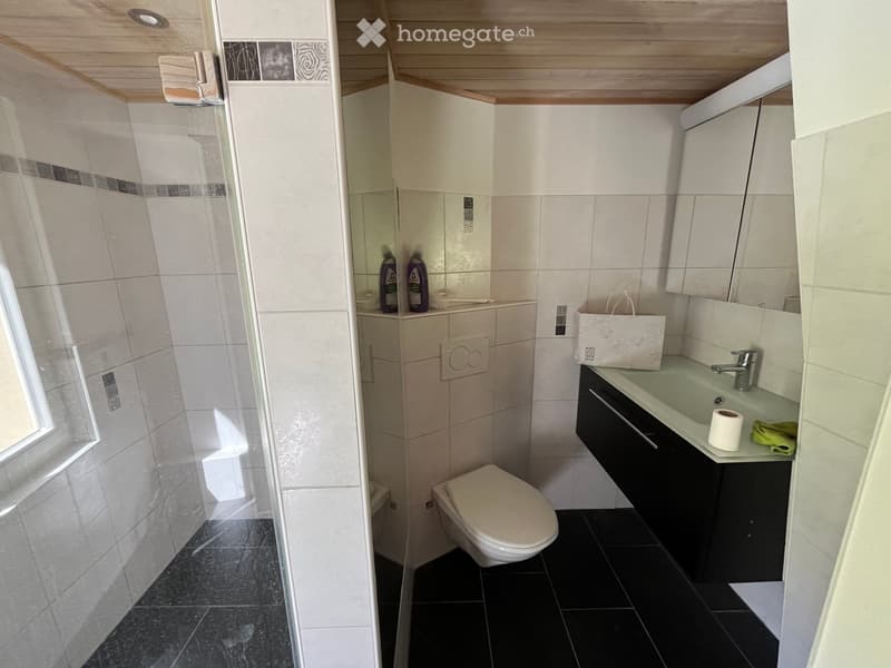 Modern bathroom with white tiles, black floor, toilet, sink, mirror, and shower area.