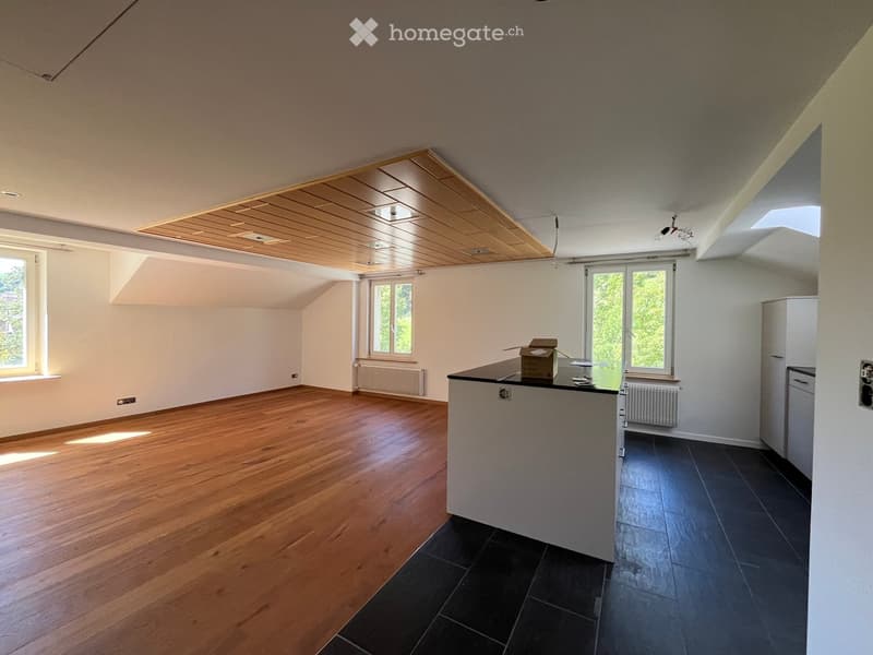 Bright, modern kitchen with wooden floors, white walls, and large windows. Features a white countertop, a refrigerator, and a small storage box on the counter.