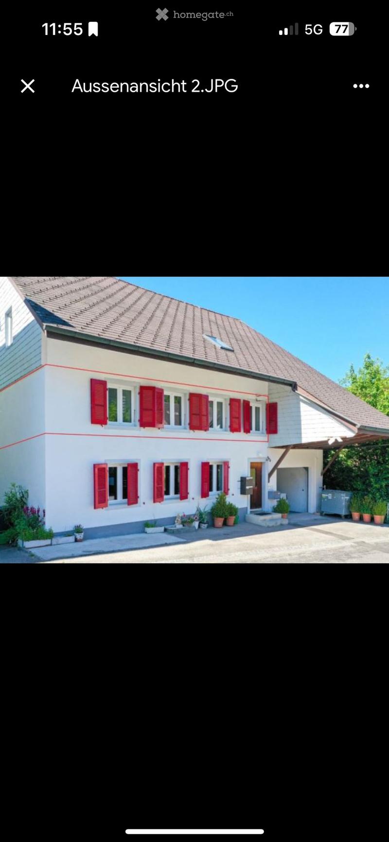 Two-story house with white exterior, red shutters, multiple windows, and a small garden area with potted plants.