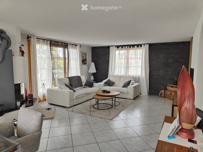 Modern living room with white sofas, a round coffee table, a side chair, and large windows with curtains. The space features a tiled floor, a decorative vase, and a side table with a lamp.