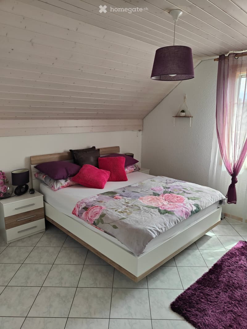 Cozy bedroom with a white wooden bed, floral duvet, nightstand, lamp, and purple rug.