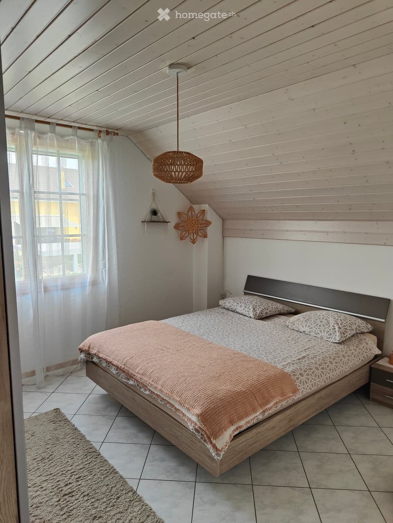 Cozy bedroom with a wooden bed, patterned bedding, a nightstand, a fluffy rug, and a hanging woven light fixture.