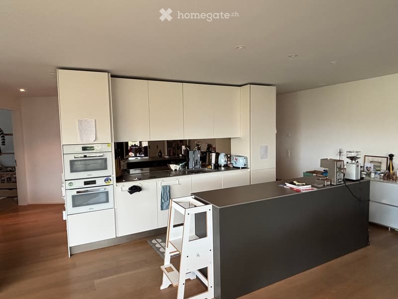 Modern kitchen with white cabinets, stainless steel appliances, and a black island countertop. Includes an oven, sink, faucet, coffee maker, and a small white stool.