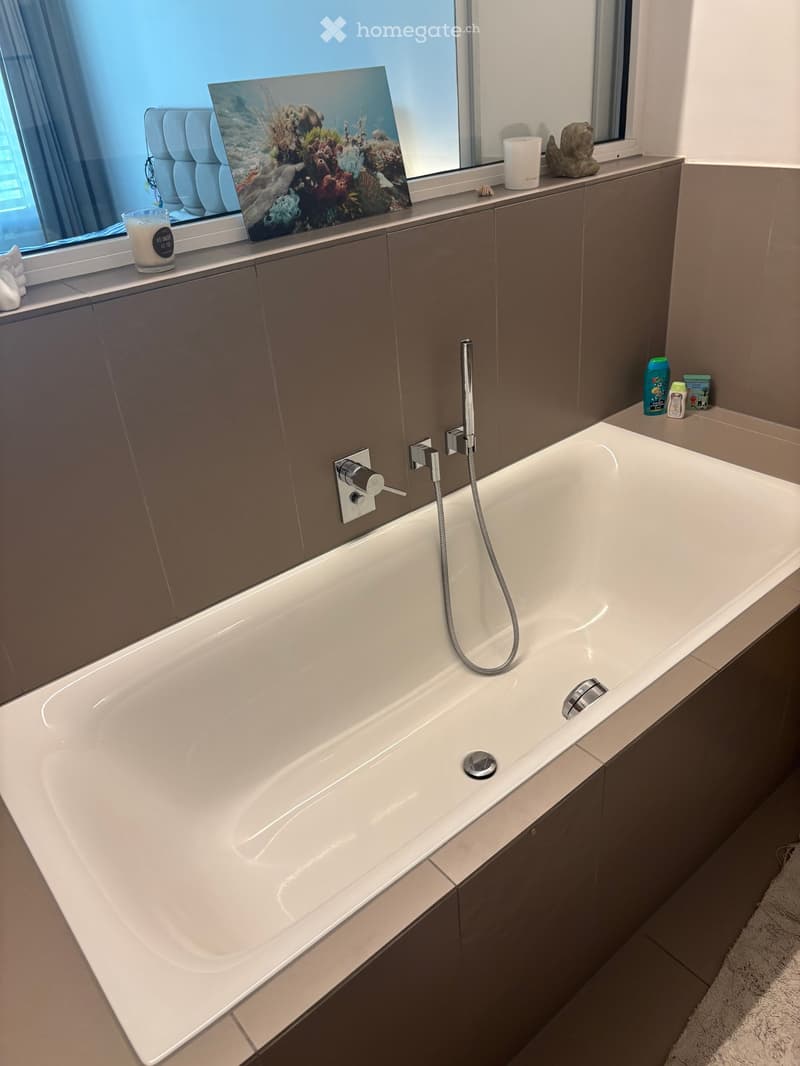 Modern bathroom with a large bathtub, sleek faucet, dark grey cabinets, and decorative items on the windowsill.