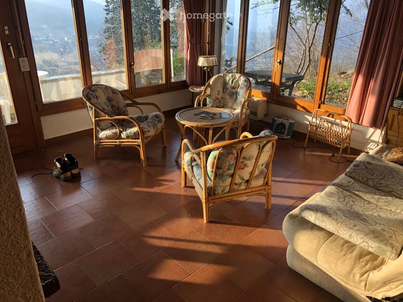 A cozy living room with large windows offering a scenic view, featuring a sofa, chairs, a small table, and a lamp.