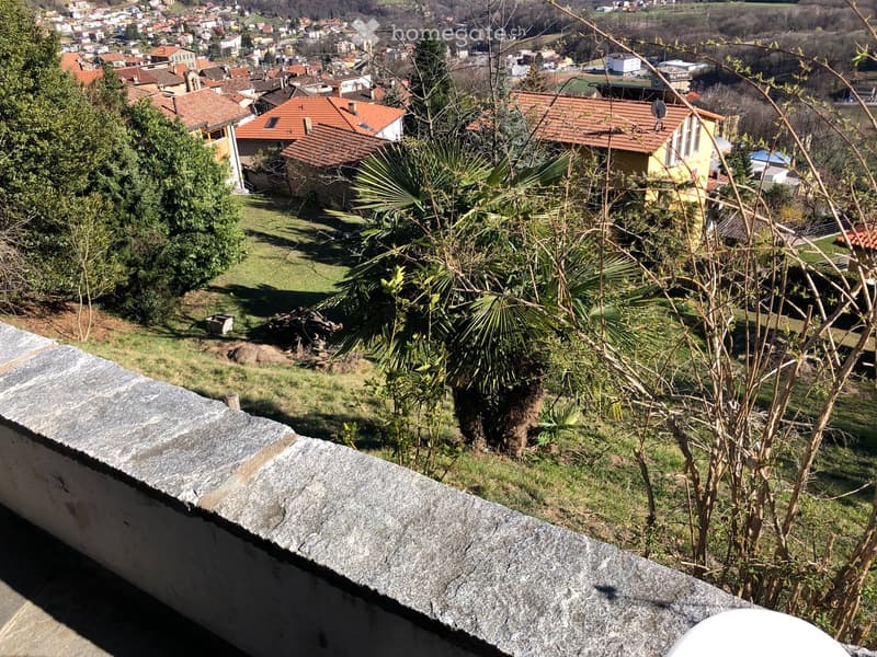 View from a balcony or terrace overlooking a residential area with houses, trees, and a green lawn.