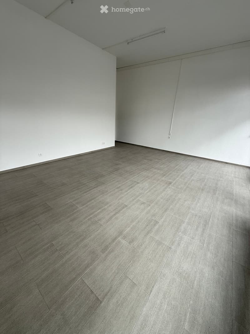 Empty room with light grey walls and a grey tiled floor, featuring a white ceiling with visible lighting fixtures.