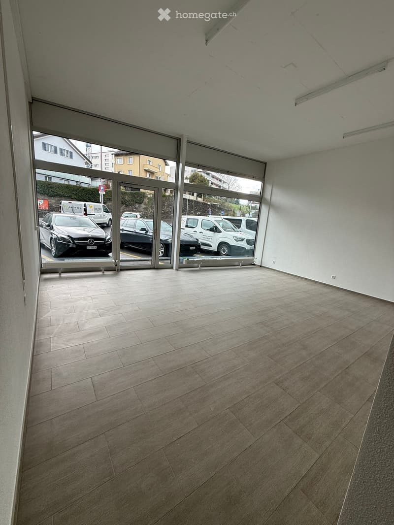 Empty room with large glass doors leading to a parking area, tiled floor, and white walls.