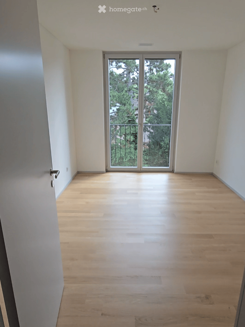 Empty room with wooden flooring and a large sliding glass door leading to a balcony.