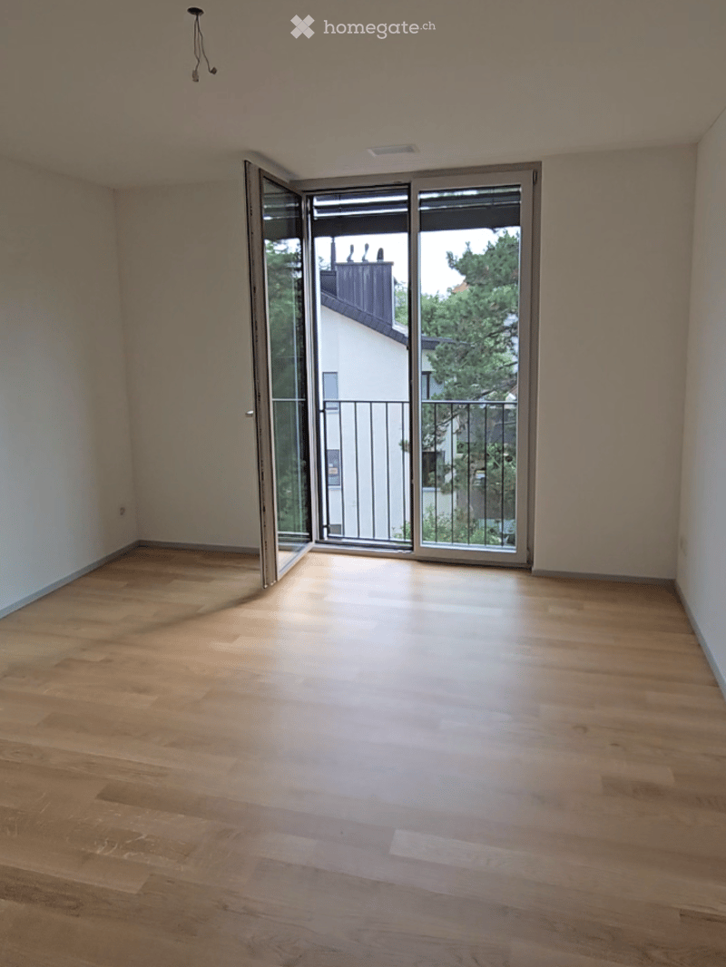 Empty room with wooden flooring, large sliding glass door leading to a balcony with metal railing and outdoor view.