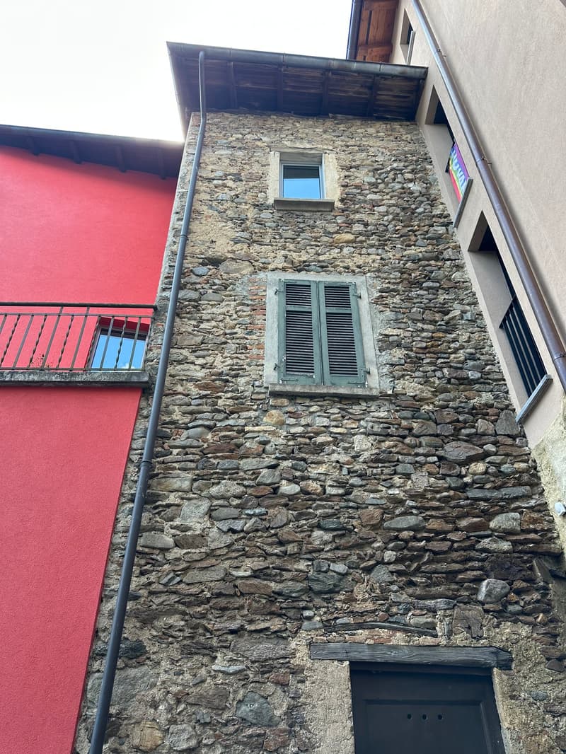 Stone building with multiple windows, shutters, and a small balcony on the left side.