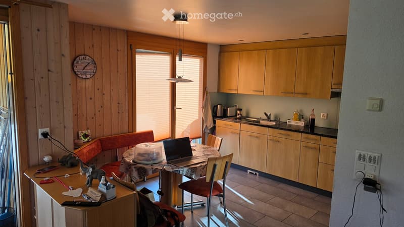A cozy kitchen and dining area with wooden cabinets, a dining table with chairs, a laptop, and various kitchen appliances.