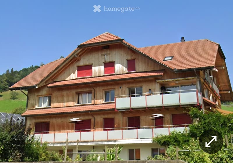 Two-story wooden house with red shutters, multiple balconies, and a red-tiled roof.