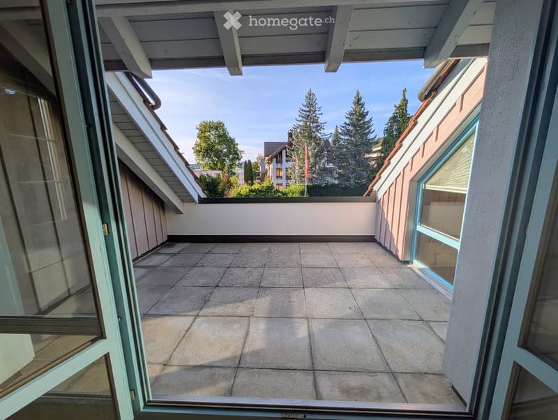 Balcony with tiled floor, glass doors, and a view of trees and neighboring buildings.