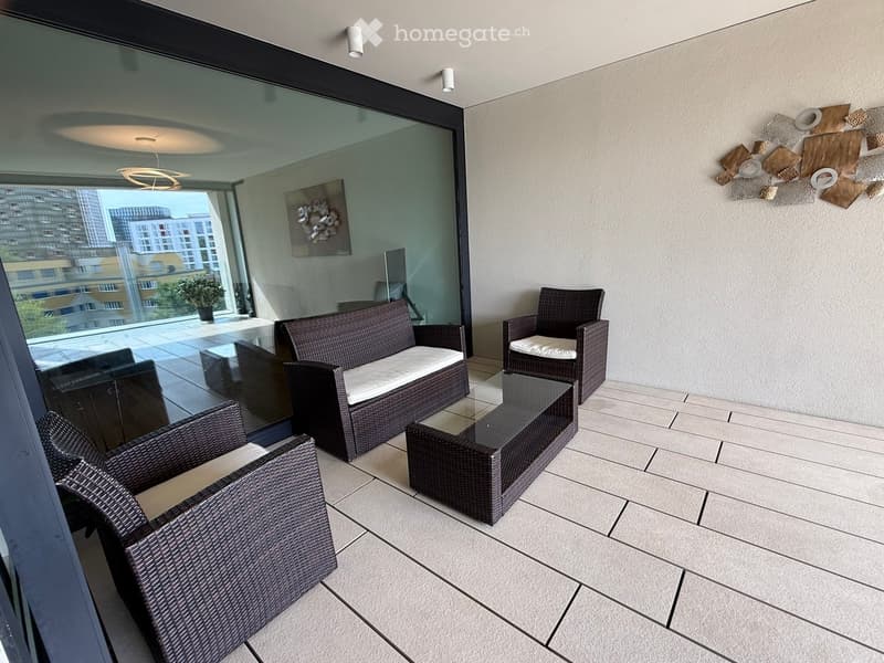 Balcony with wicker furniture, including a sofa, chairs, and a coffee table, with a view of the city.
