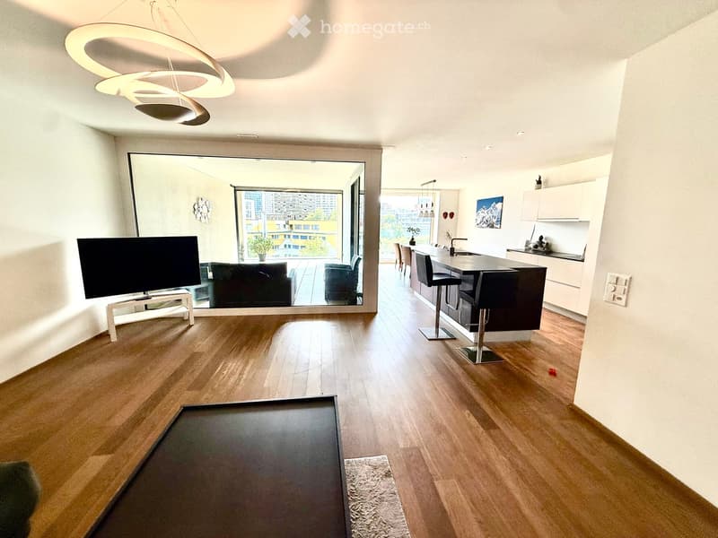 Open-plan living and dining area with a modern sofa, chairs, a coffee table, a kitchen island with stools, and a pendant light fixture.