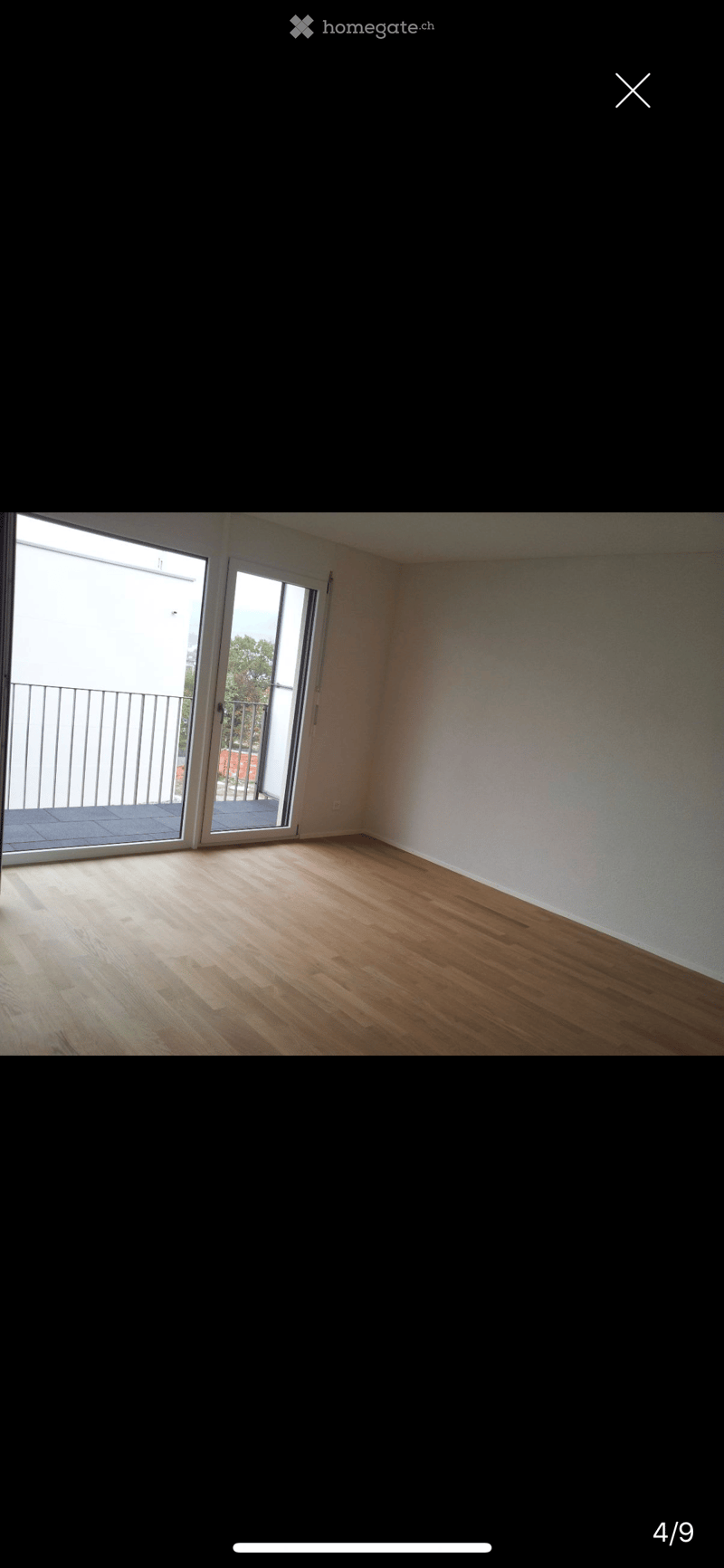 Empty room with wooden flooring, white walls, and large sliding glass doors leading to a balcony.